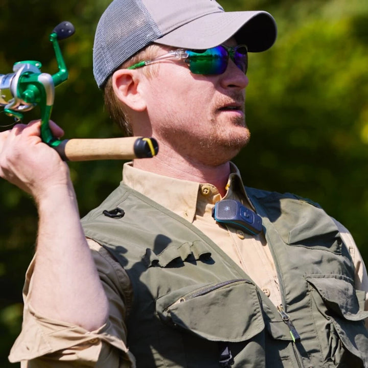 Man fishing outdoors while wearing the NoxGear 39g Bluetooth speaker clipped to his vest, perfect for outdoor activities.