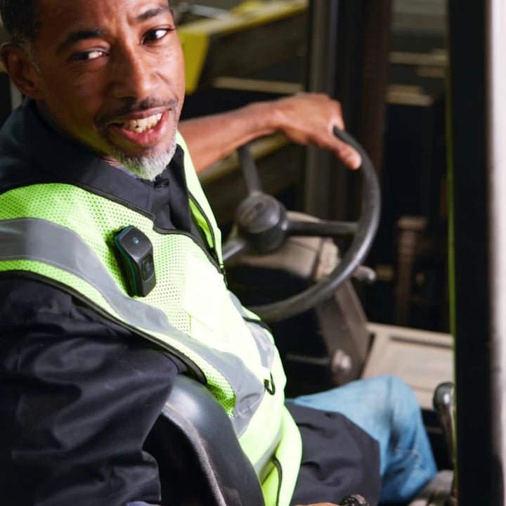 Worker operating a forklift with the NoxGear 39g Bluetooth speaker securely clipped to his safety vest.