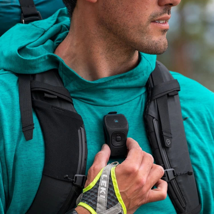 Hiker using the magnetic clip on the NoxGear 39g Bluetooth speaker, perfect for outdoor adventures.