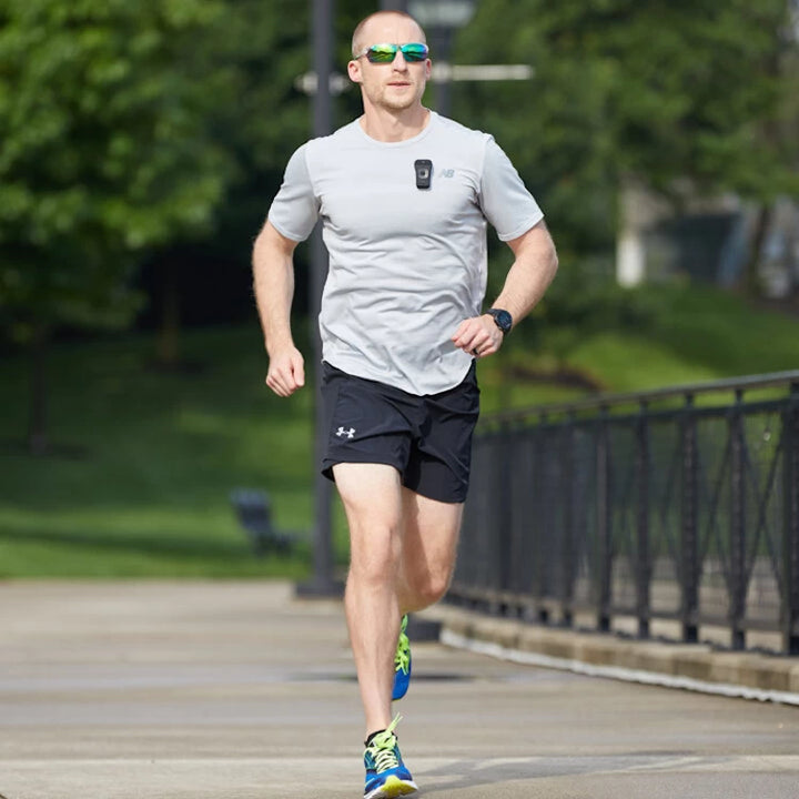 Runner in a park wearing the NoxGear 39g Bluetooth speaker clipped to a shirt, showcasing its no-bounce design.