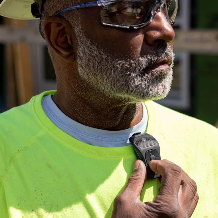 Worker clipping the NoxGear 39g Bluetooth speaker onto a neon work shirt, ideal for job sites.