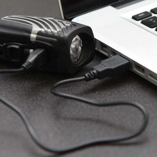 NiteRider Lumina 1000 Boost LED headlight charging via USB connected to a laptop.