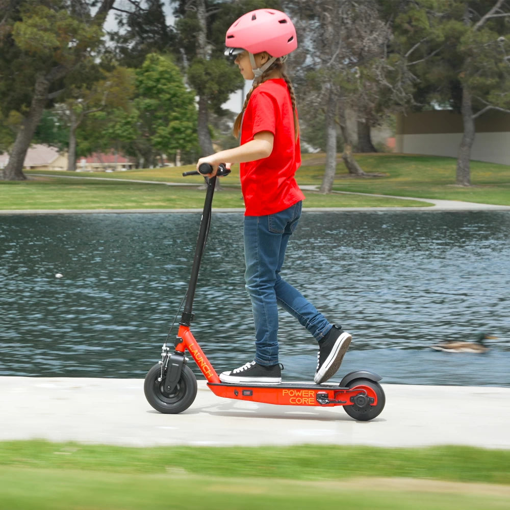 Left side view of a child riding the Razor PowerCore Launch electric scooter by a lake, ideal for children aged 8+ years, promoting safe outdoor fun.