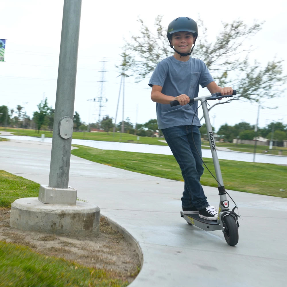 Teen riding Razor PowerCore Siege Electric Scooter through a park, designed for ages 13+, with a high-torque rear hub motor.