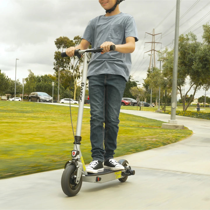 Teenager riding Razor PowerCore Siege Electric Scooter on smooth pavement, suitable for kids aged 13+, max weight of 70 kg.