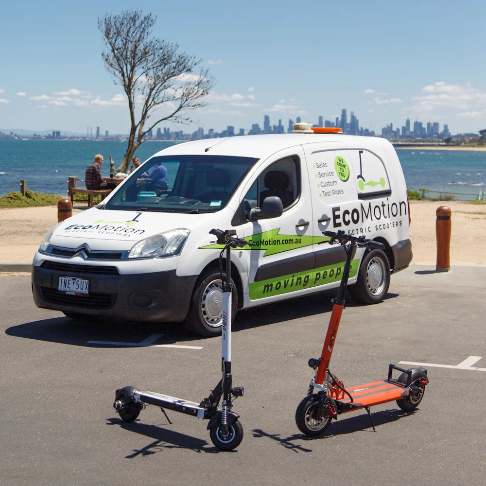 EcoMotion van parked along Port Phillip Bay, with Melbourne on the horizon, showcasing the EMOVE Touring and EMOVE Cruiser demo electric scooters. The image highlights EcoMotion’s mobile service, offering free test rides at your home or workplace, as well as convenient pickup and delivery options across Melbourne, Geelong, and Regional Victoria.