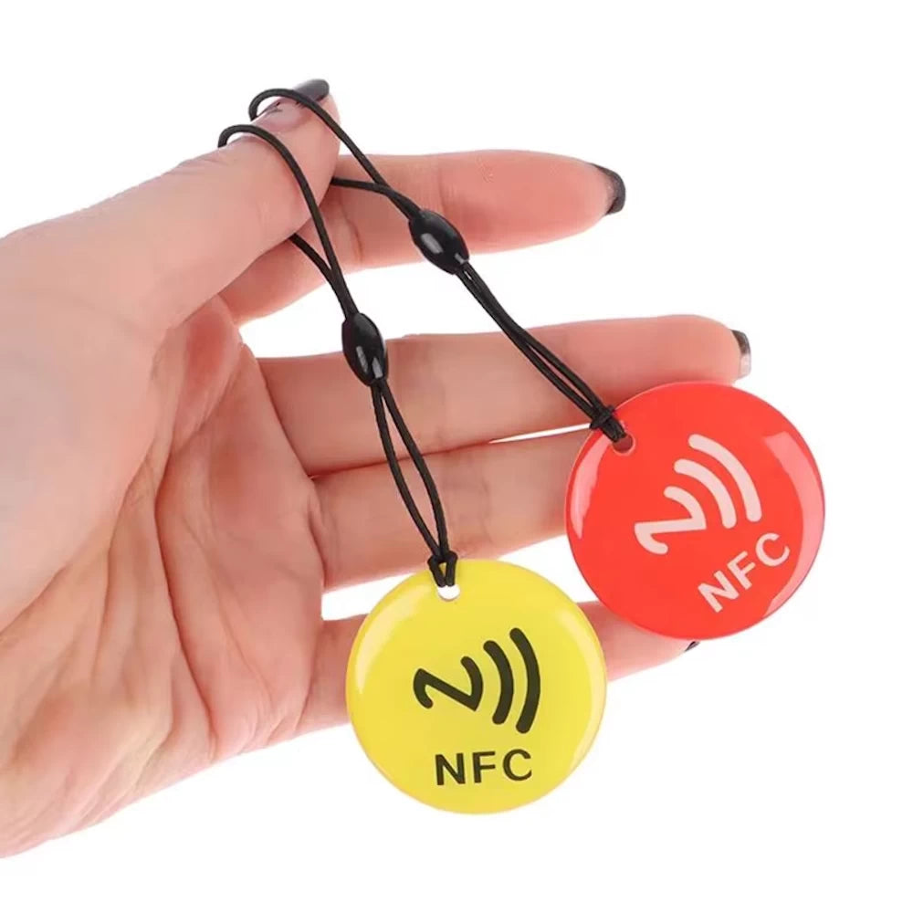 Hand holding two NFC tag tokens in yellow and red, showcasing portable and durable design for electric scooter NFC security.