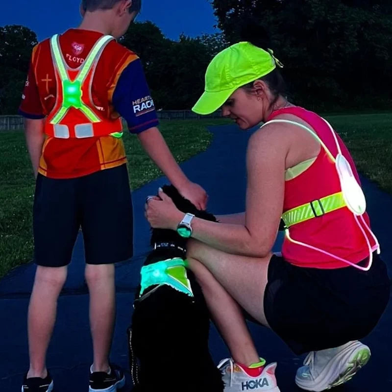 A mother and son wear their Tracer2 and TracerJR LED vests while exercising after dark with their dog, which is wearing a LightHound LED Safety Harness.