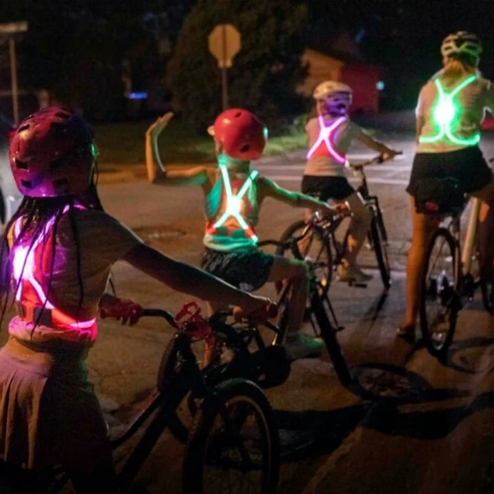 A mother and children riding bikes at dusk, all wearing TracerJR LED safety vests with glowing LED lights for visibility on roads.