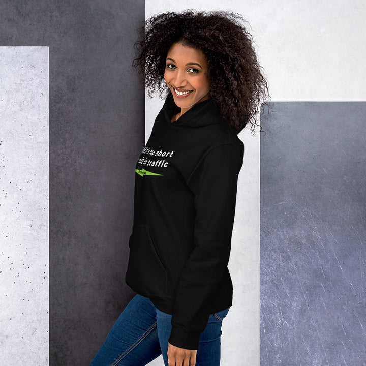 Smiling woman wearing the "Life's Too Short To Sit In Traffic" EcoMotion hoodie in black, standing against a modern abstract background.